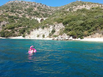 Siblings with inflatable swimming in lake against mountains