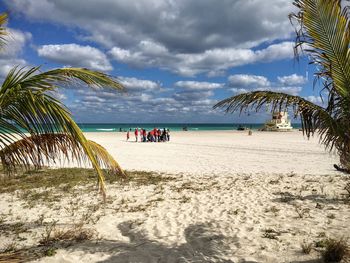 Tourists on beach against cloudy sky