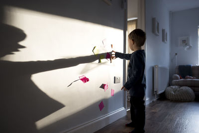 Full length of boy sticking adhesive notes on wall at home