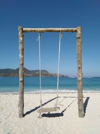 Wooden swing on beach against clear blue sky