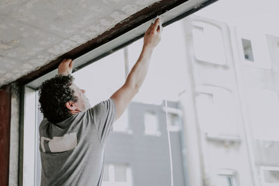 A young caucasian man repairing a window opening while and cleaning the frames with a knife