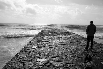 Rear view of man standing on pier at sea against cloudy sky