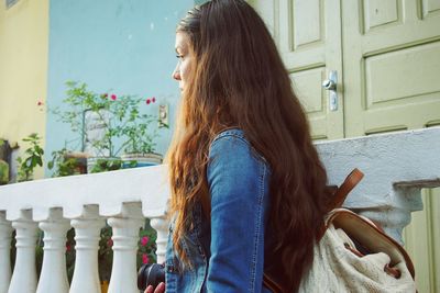 Side view of young woman carrying bag against house