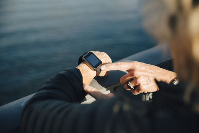 Cropped image of senior woman using smart watch at bridge railing