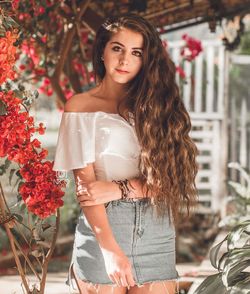Portrait of beautiful young woman standing by flower plants