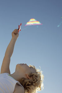 From below unrecognizable cute little boy with curly blond hair launching colorful kite under cloudless blue sky on sunny summer day