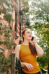 Young woman using phone while standing on tree