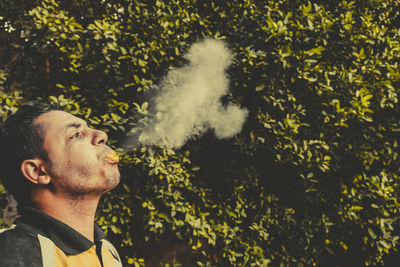 Young man smoking against trees