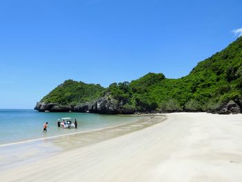 People on beach against clear blue sky