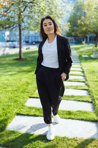 Full body portrait of asian confident business woman in suit, walking in business center spring park