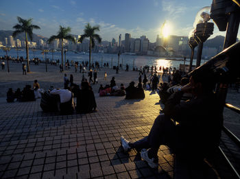 People on beach in city against sky during sunset