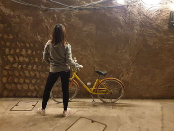 Rear view of woman with bicycle standing against wall