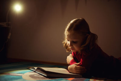 Girl reading book while lying on carpet at home