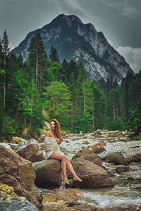 Woman sitting on rock against mountains in forest