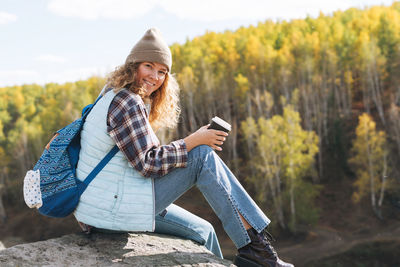 Young woman with curly hair in plaid shirt, jeans looks at magic view of mountains and river