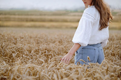 Woman walking on wheat golden field holding heap of rye. fashionable female touching wheatear
