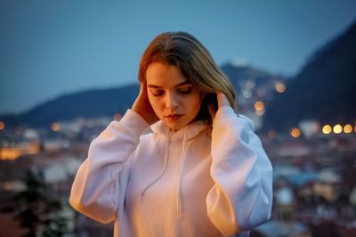 Young woman looking away while standing against sky at dusk