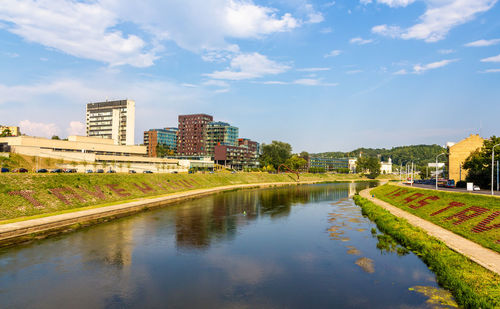 Canal by buildings in city against sky