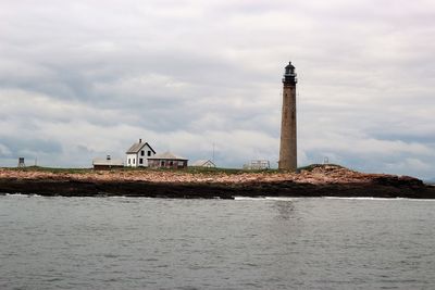 Lighthouse by building against cloudy sky