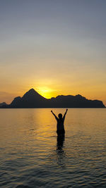 Silhouette person in sea against sky during sunset