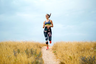 Full length of young woman jogging on grassy land