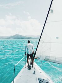 Rear view of man standing boat in sea against sky