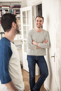 Young gay man standing arms crossed while looking at partner in house