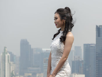 Side view of young woman looking at city against sky