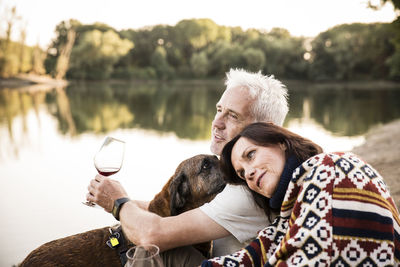 Relaxed senior couple with dog and wine at a lake