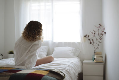 Woman in white shirt sitting back to camera on the bed