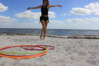 Full length of young woman at beach against cloudy sky