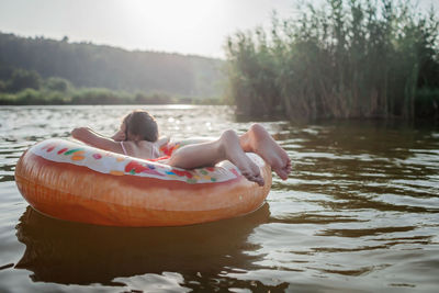 Girl relaxes on big donut inflatable ring on lake on hot summer day, happy summertime, countryside