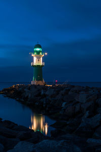 Lighthouse by sea against sky at night