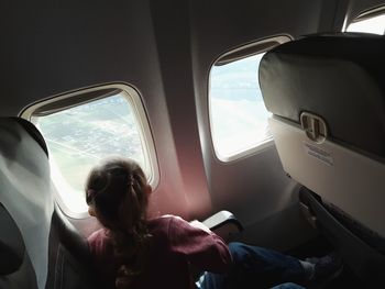 Rear view of a little girl sitting on an airplane looking out the porthole
