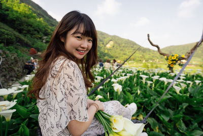 Portrait of smiling young woman wearing hat holding flower on field