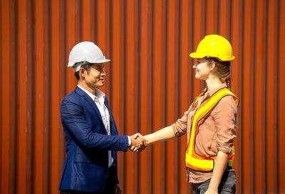 Colleagues wearing hardhat giving handshakes while standing against cargo container