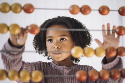 Schoolgirl with curly hair learning to count using abacus in classroom at kindergarten