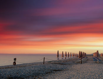 Rows of closed umbrellas on the beach at dramatic colorful sunrise