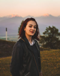 Portrait of smiling young woman standing in park during sunset