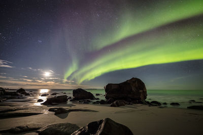 Scenic view of rocks at beach against aurora polaris in sky at night