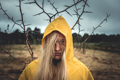 A girl with long hair in a yellow hood, with the back of a tree with thorns mysticism, dark thoughts