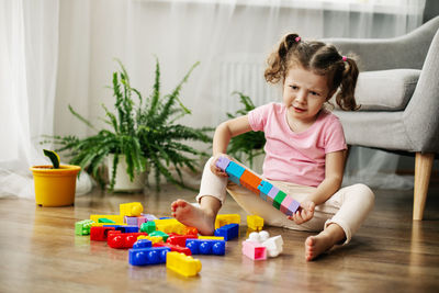 A little girl is sitting on the floor in the playroom and playing with colorful cubes