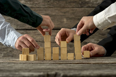 Cropped hands of business people arranging wooden blocks on table