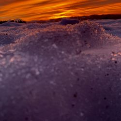 Surface level of frozen beach against sky during sunset