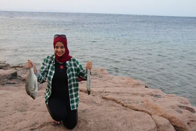 Portrait of smiling woman holding fish at beach