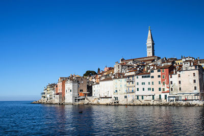 Croatian city by the sea with a church and steeple on the right.