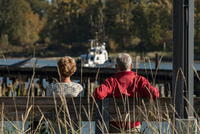 Rear view of people sitting on bench against lake