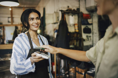 Smiling female owner assisting customer doing online payment at workshop