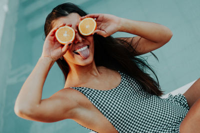 High angle portrait of young woman holding orange while sitting at poolside