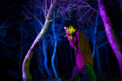 Side view of man smoking cigarette while walking by illuminated trees in forest at night